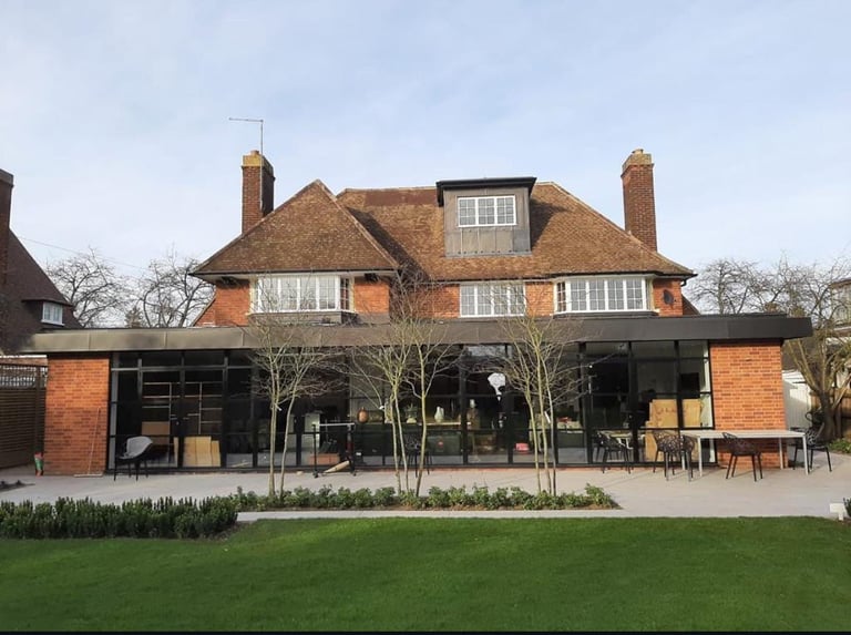 Modern brick house with mansard roof and contemporary dark glass extension featuring a patio area and manicured lawn