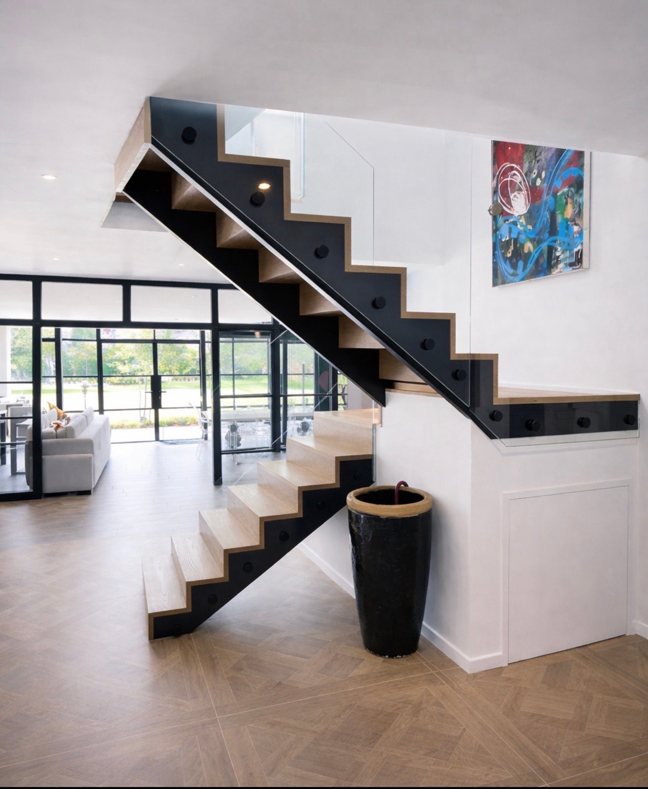 Modern staircase with black and wood steps, metal railings, and artwork on white walls in a bright open-plan interior space