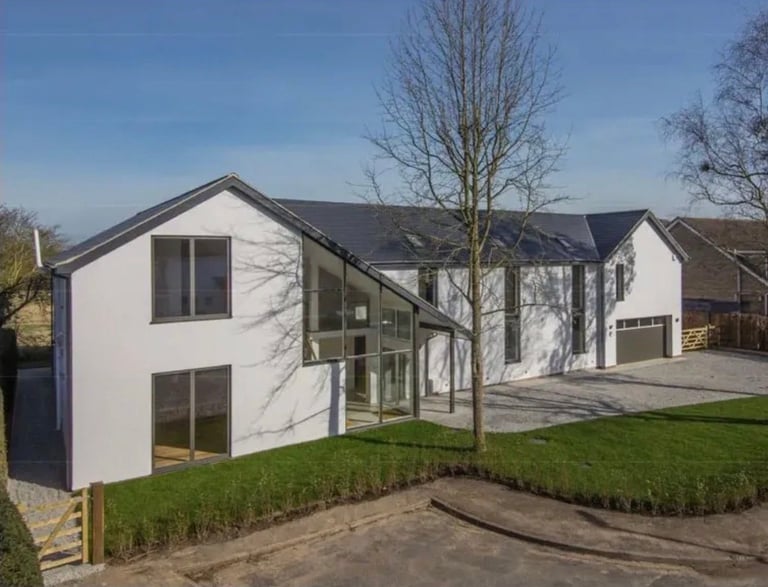 Modern white residential house with angled roof, large windows, and garage, surrounded by green lawn and bare trees