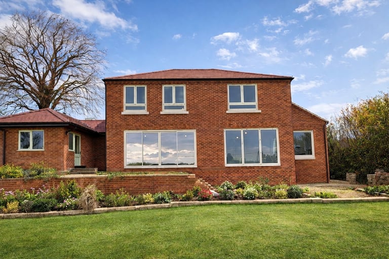 Modern brick house with large windows, manicured lawn, and bare trees under blue sky with clouds