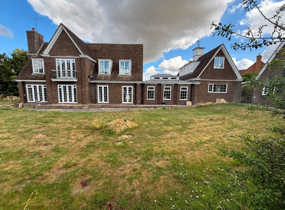 Large brick residential house with manicured lawn and blue sky, viewed from the front garden