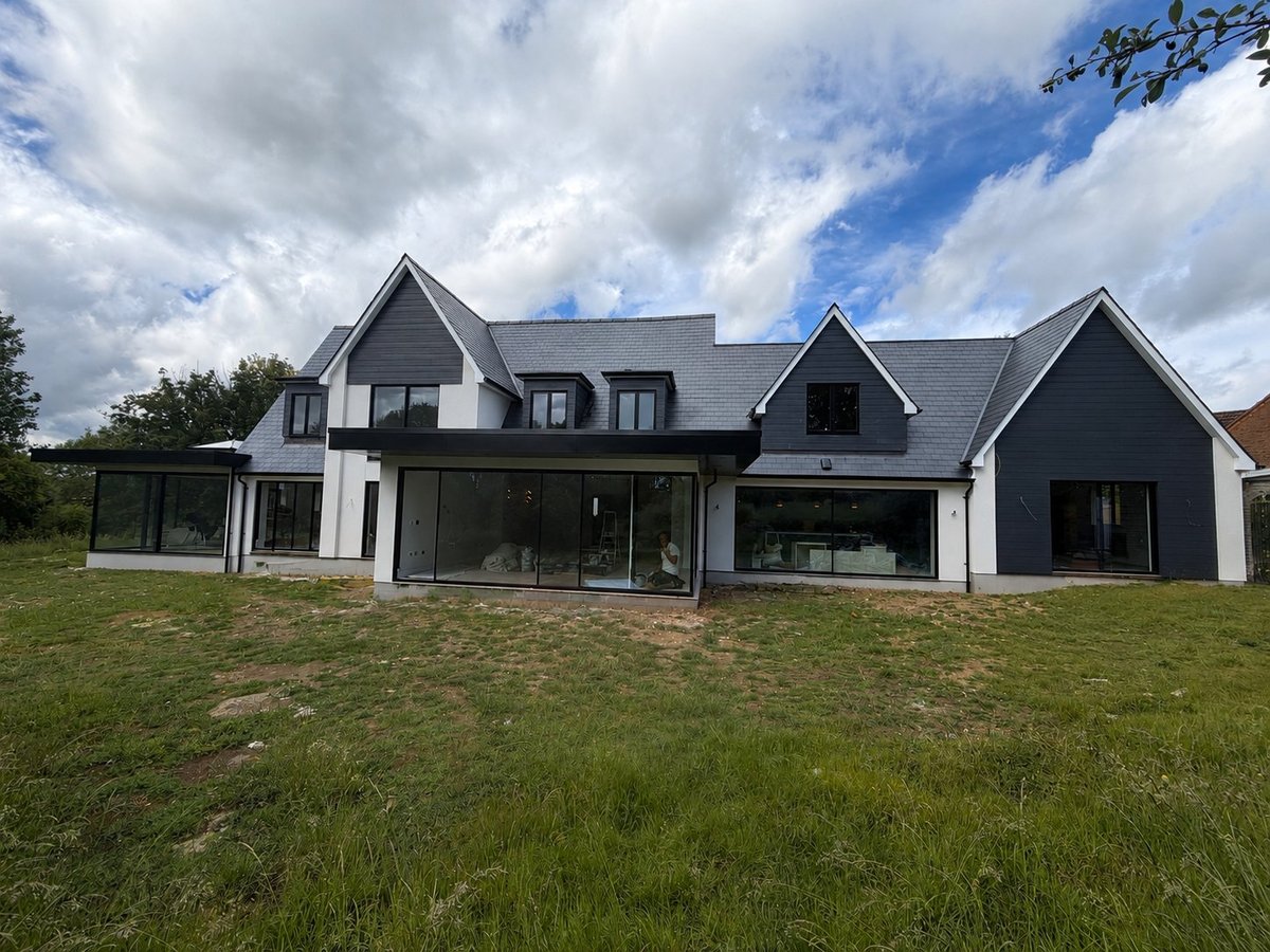 Modern two-story house with black and white exterior, gabled roof, and large windows, set on a grassy lawn under cloudy sky