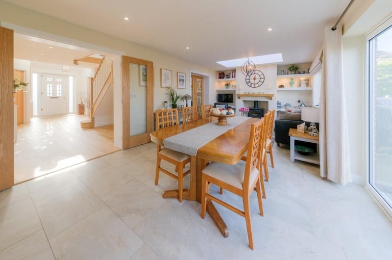 Bright open-plan kitchen and dining area with wooden table, chairs, light tile flooring, and modern appliances