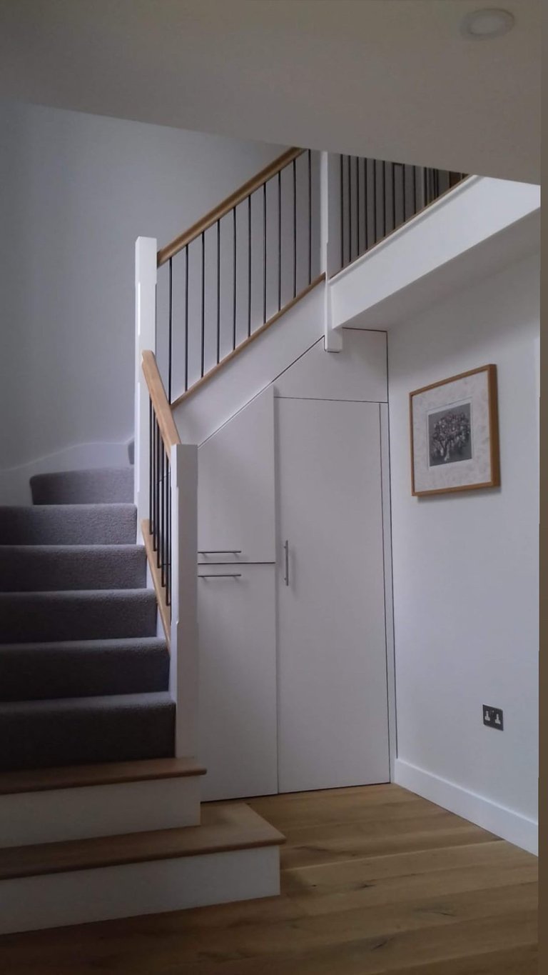 Modern staircase with wooden steps and metal railing leading to upper floor, white walls with framed artwork