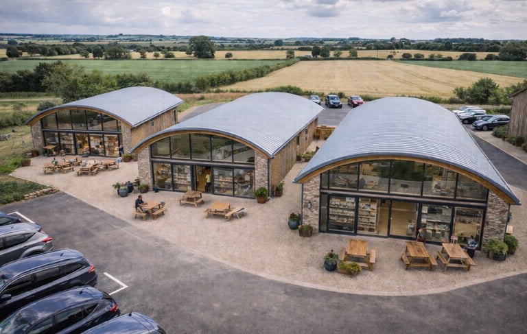 Aerial view of a modern architectural complex with white curved barrel-vaulted roofs and glass facades set in a rural agricultural landscape