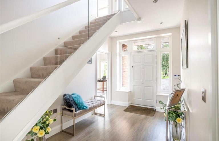 Bright modern entryway with wooden staircase, white walls, bench seating, potted plants, and white front door with glass panes