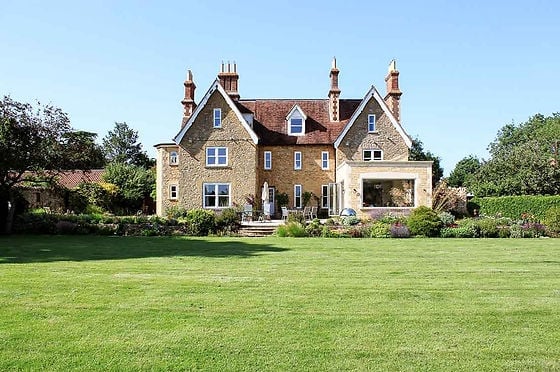 Victorian brick mansion with ornate chimneys set on a manicured lawn surrounded by trees and countryside