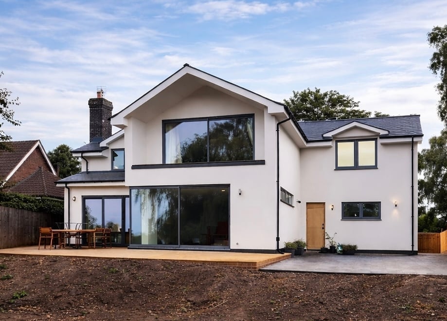 Modern two-story white house with large windows, brick chimney, and wooden deck against blue sky