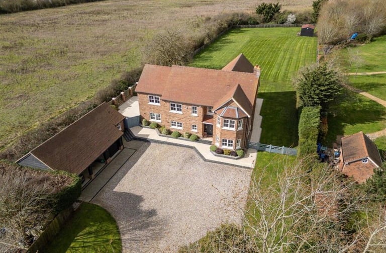 Aerial view of a brick country house with terracotta roof, driveway, and surrounding fields