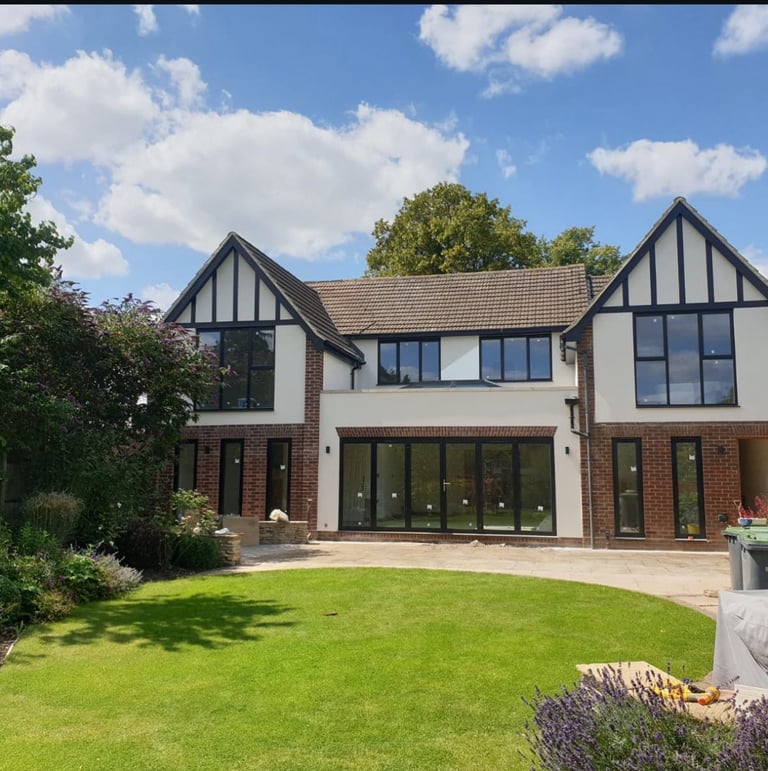 Modern Tudor-style house with brick and white facade, large green lawn, and manicured garden landscaping