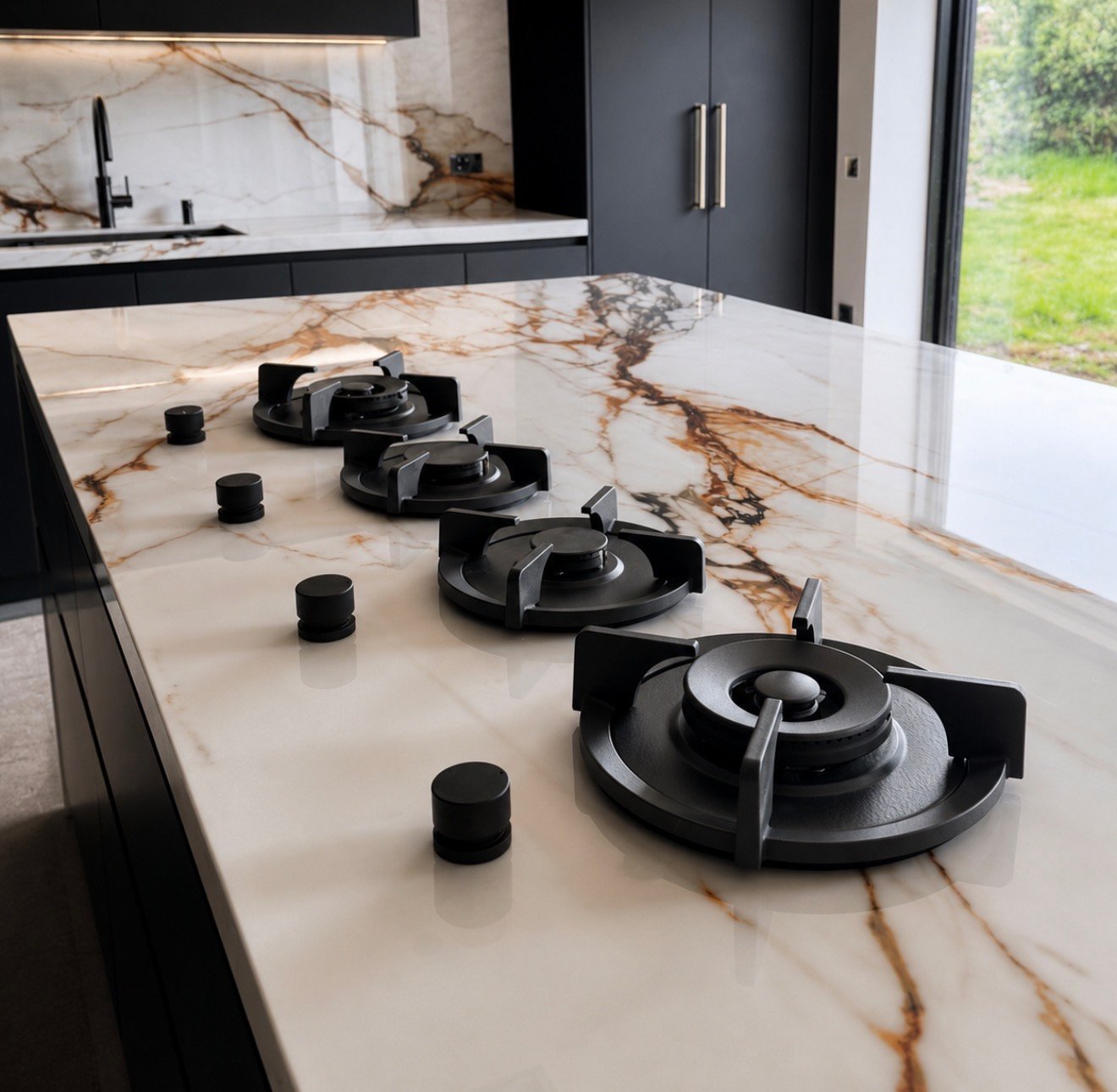 Modern kitchen island with white and gold marble countertop displaying black gas cooktop burners and black cylindrical knobs
